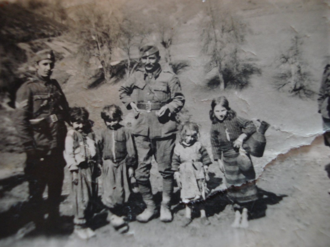 Χωριό Στρενάτι, Αλβανία, 25-03-1941. Αριστερά ο λοχίας Βασίλης Σαββανάκης και δεξιά ο επίσης Βελεστινιώτης Γιάννης Παπατόλιας. Δεξιά η μικρή κοπέλα ονομάζεται Σιανίκω και μαζί με τις υπόλοιπες βοηθούσαν τους Έλληνες στρατιώτες. Στο χωριό αυτό που δεν είχε και πολύ στρατό, βρήκαμε πιο εύκολα γάλα, αυγά, κότες κλπ. που είχαμε μεγάλη ανάγκη για να συνέλθουμε και να δυναμώσουμε. Θυμάμαι που μας εξυπηρετούσαν πρόθυμα μερικά κορίτσια 5-7 χρονών, που έχω σε κάτι φωτογραφίες που βγήκαμε στις 25 Μαρτίου. Η μία μάλιστα λεγόταν Σιανίκω. Ήταν η πιο πρόθυμη και μάζευε τις άλλες και τις έβαζε να μας φέρουν νερό από τη βρύση, να μας πλένουν τις καραβάνες, να μας αγοράζουν αυγά, τυρί κ.λ.π. που πρόθυμα το έκαναν επειδή υποφέραμε πολύ στο Μνήμα της Γριάς. Θυμάμαι τις δύο δίδυμες αδελφούλες 5 ετών, που έχω και στη φωτογραφία και ήταν σωστά αγγελουδάκια. Δεν συγκρατώ όμως τα δύσκολα αλβανικά ονόματά τους. Β. Σαββανάκης, Γκοροτόπι, μνήμες και βιώματα του πολέμου στην Αλβανία, επιμ. Π. Καμηλάκης, Σύλλογος Βελεστινιωτών Αθήνας, Αθήνα, 1987, σ. 85